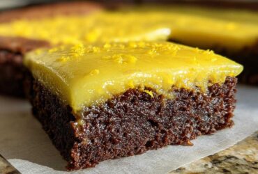 Close-up of a fudgy, dark chocolate Lemon Brownies square topped with a thick, glossy yellow lemon glaze and zest.
