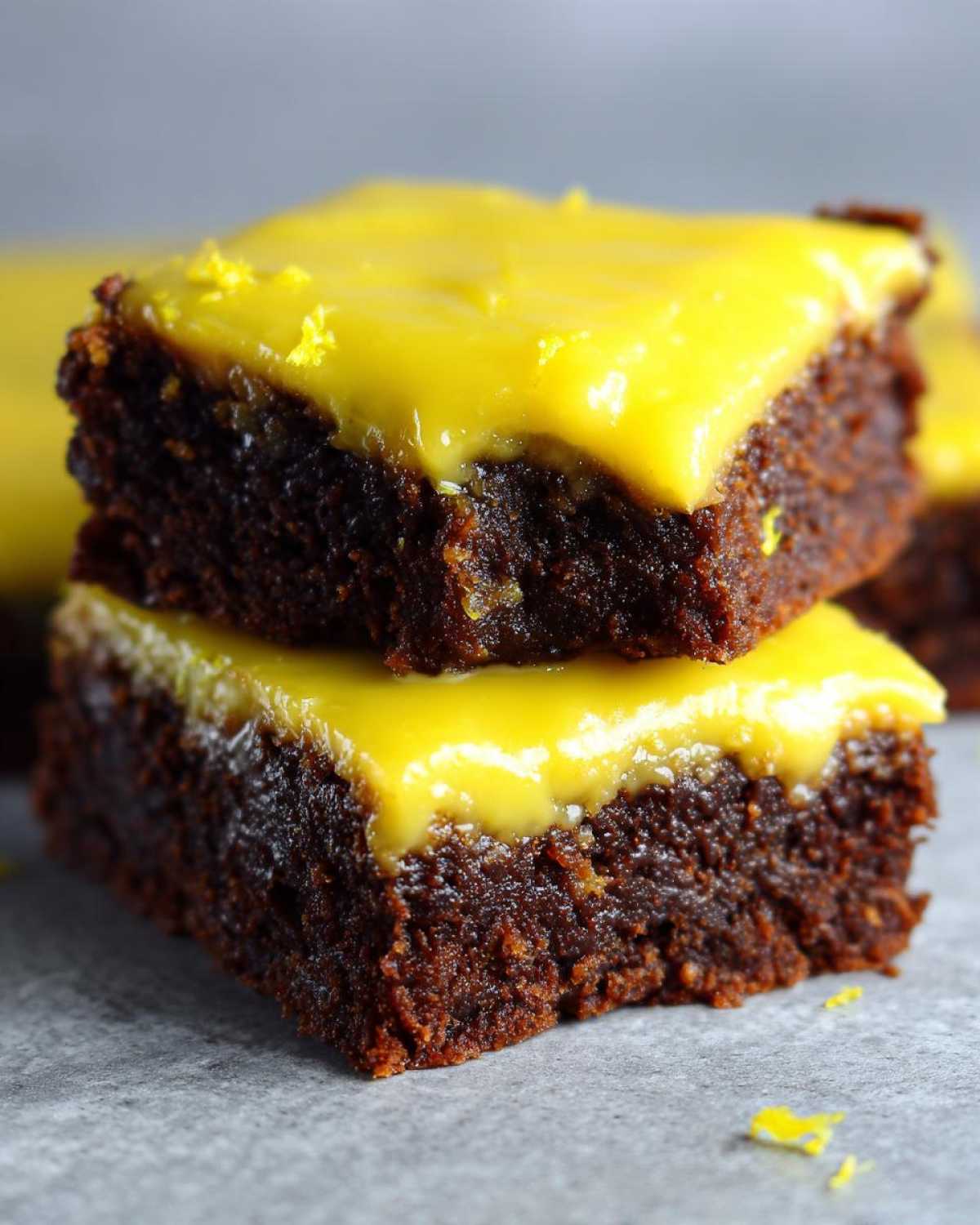 Two fudgy Lemon Brownies stacked, topped with a vibrant, glossy yellow lemon glaze and zest.
