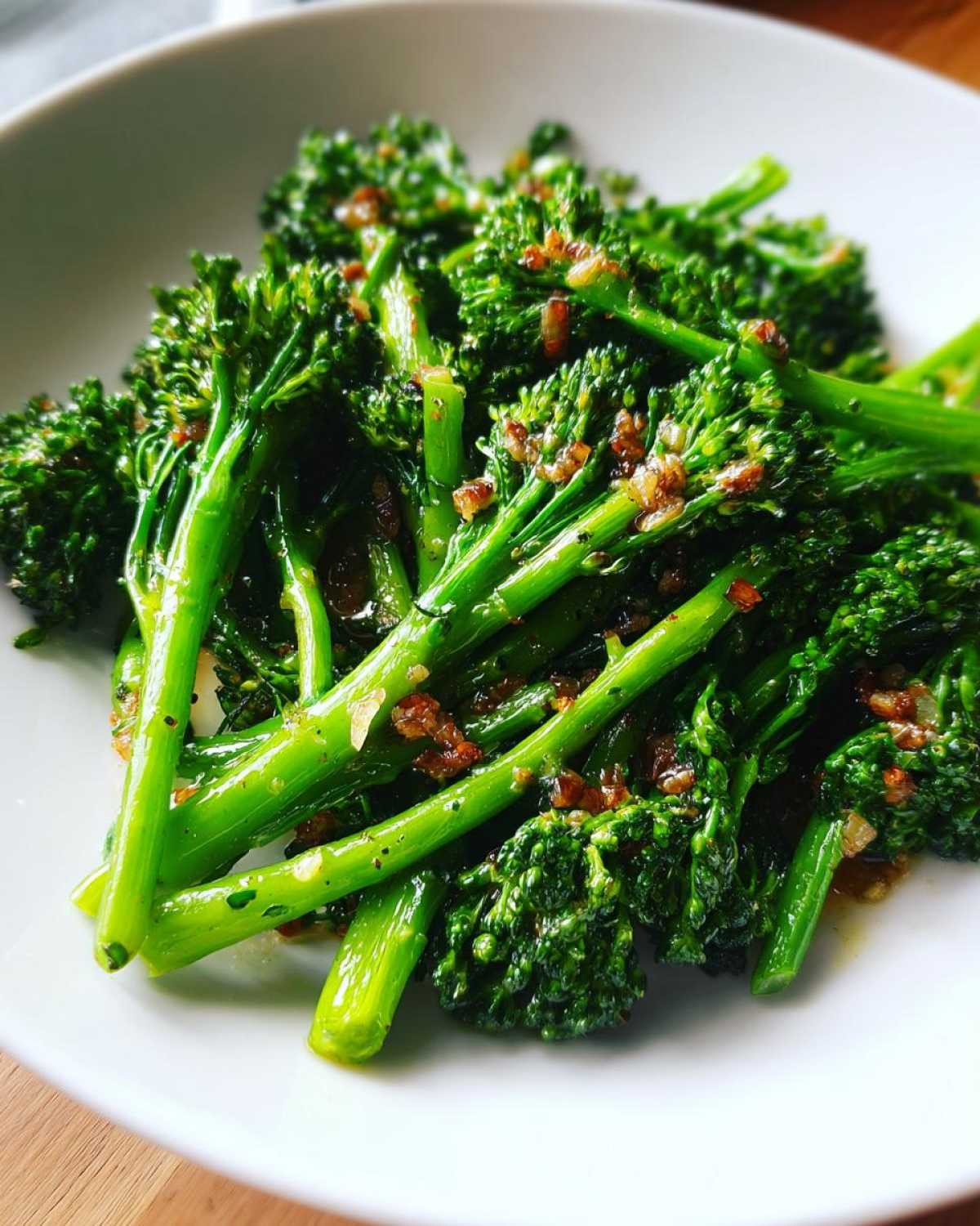 Close-up of bright green, sautéed broccolini tossed with garlic and lemon sauce in a white bowl.