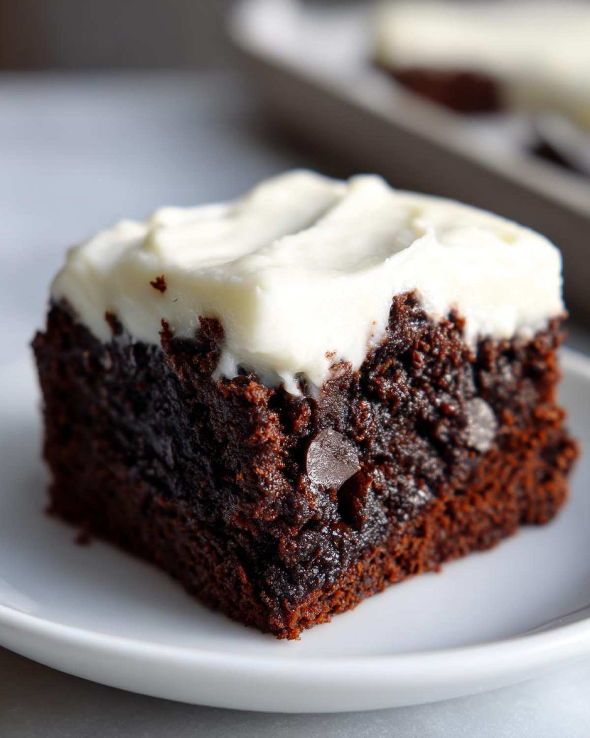 Close-up of a rich, dark gingerbread brownies square topped with thick white cream cheese frosting.