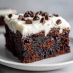 Close-up of a fudgy gingerbread brownies slice topped with white frosting and chocolate chips.