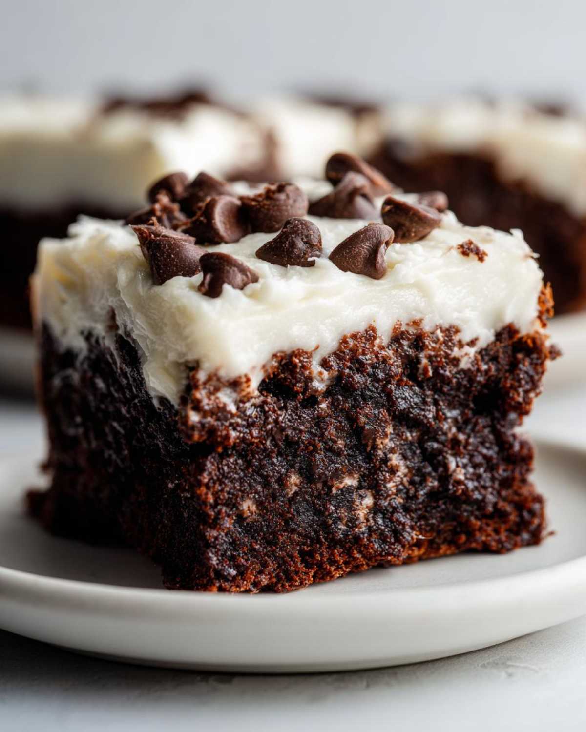 A decadent square of rich, dark gingerbread brownies topped with thick white frosting and chocolate chips.