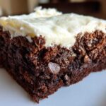 Close-up of a rich, dark slice of gingerbread brownies topped with thick cream cheese frosting.