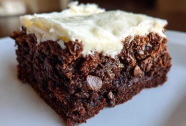Close-up of a rich, dark slice of gingerbread brownies topped with thick cream cheese frosting.