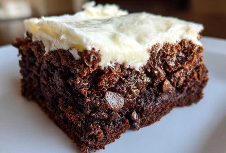 Close-up of a rich, dark slice of gingerbread brownies topped with thick cream cheese frosting.
