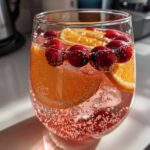 Close-up of a glass filled with sparkling pink champagne punch, garnished with orange slices and fresh cranberries.