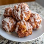 Close-up of several golden brown baked apple fritters drizzled generously with white vanilla glaze.