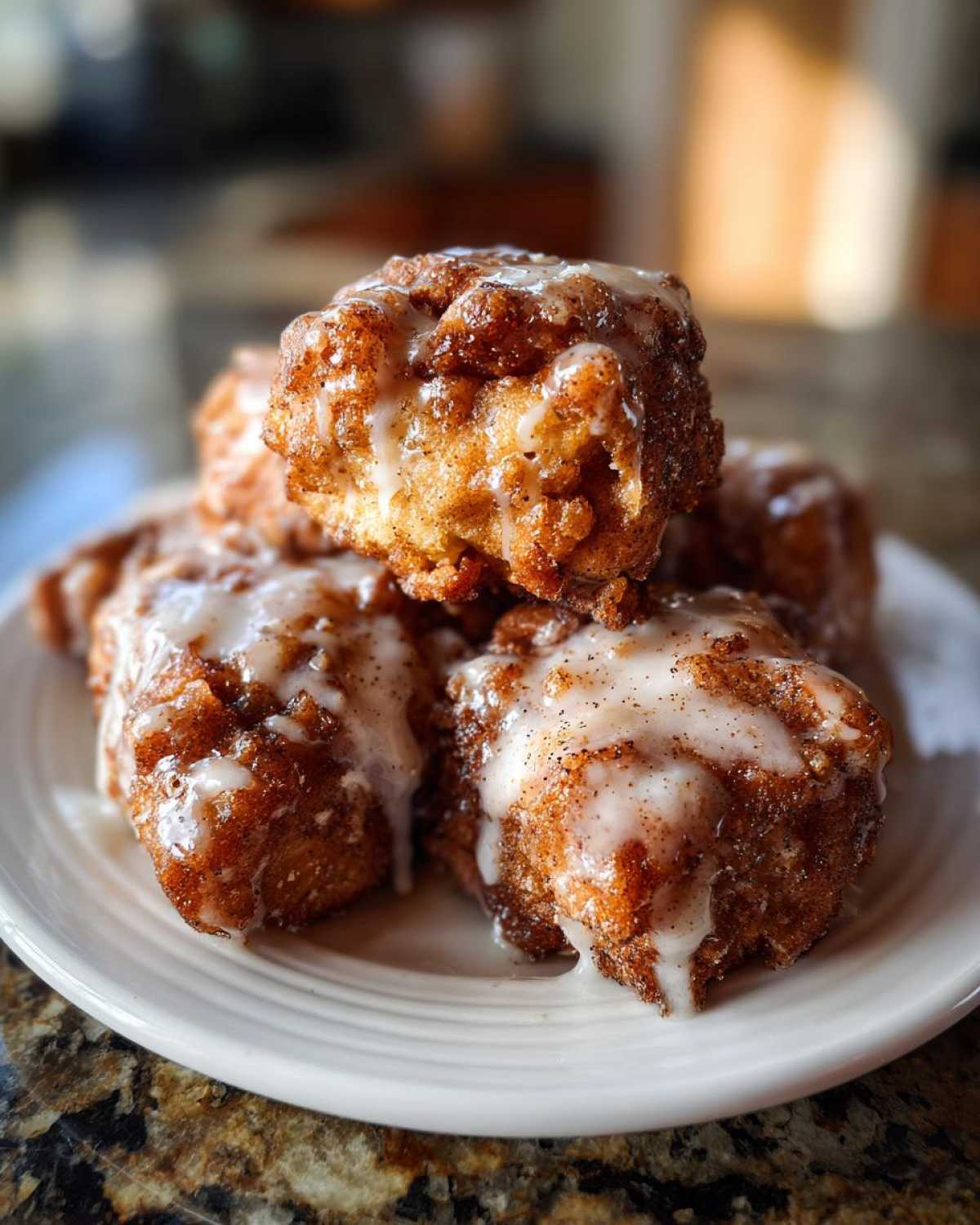 Close-up of several golden brown baked apple fritters stacked on a white plate, drizzled with white vanilla glaze.