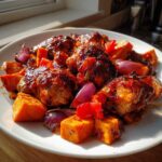Close-up of glazed harissa chicken pieces served with roasted sweet potatoes and red onions on a white plate.