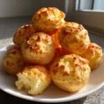 A pile of freshly baked, golden-brown brazilian cheese bread rolls on a white plate, showing a chewy interior.