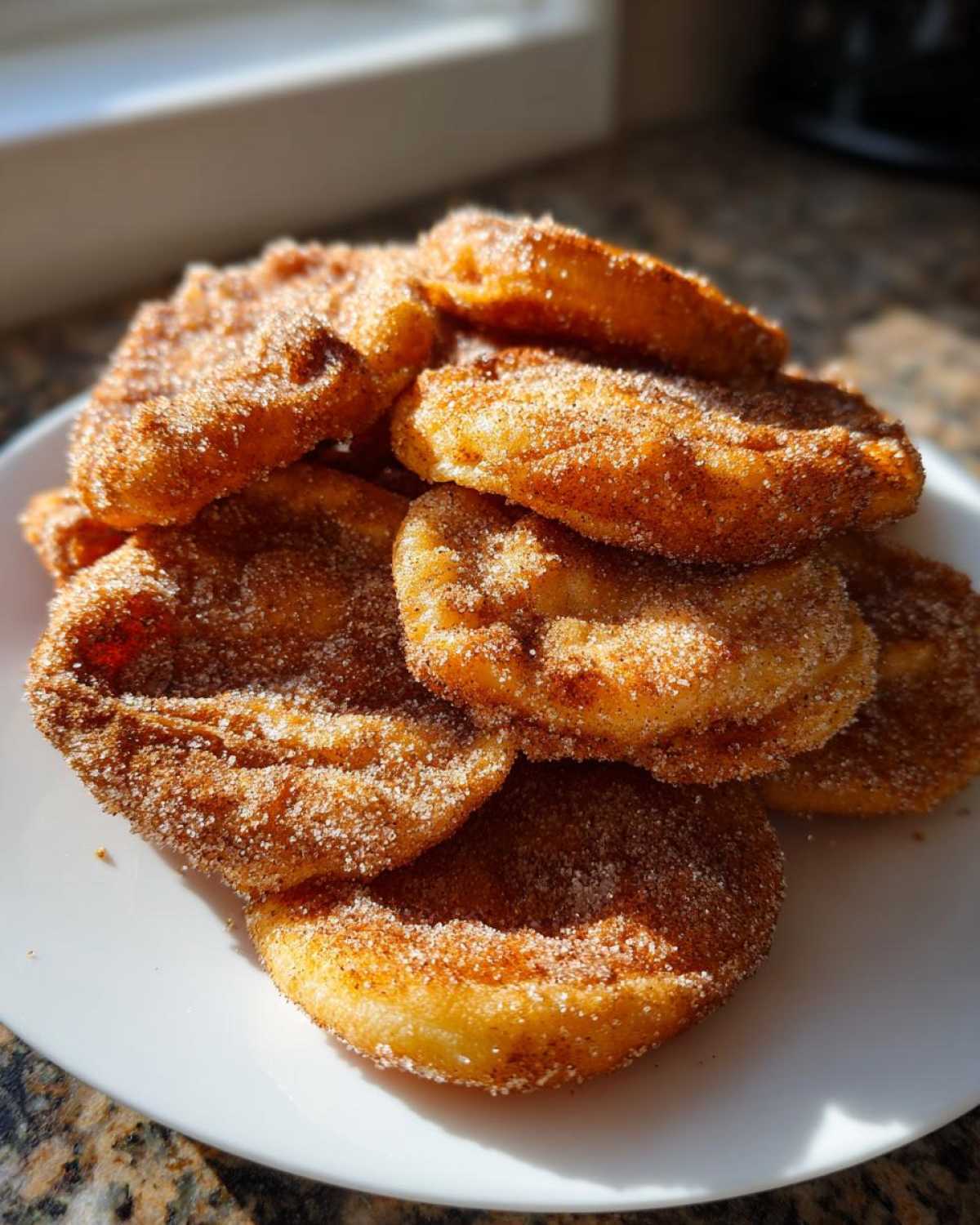 A pile of freshly made buñuelos dusted heavily with cinnamon sugar resting on a white plate.