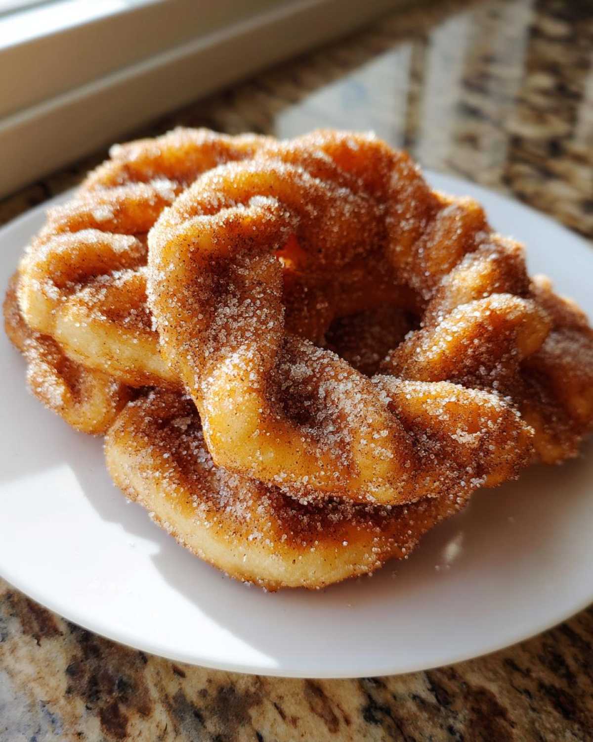 Two golden, fried buñuelos heavily coated in cinnamon sugar resting on a white plate.