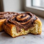 Close-up of a soft, fluffy chocolate cinnamon rolls with a bite taken out, showing the rich chocolate swirl filling.