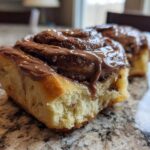 Close-up of a soft, fluffy chocolate cinnamon rolls slice topped with thick, melted chocolate frosting.