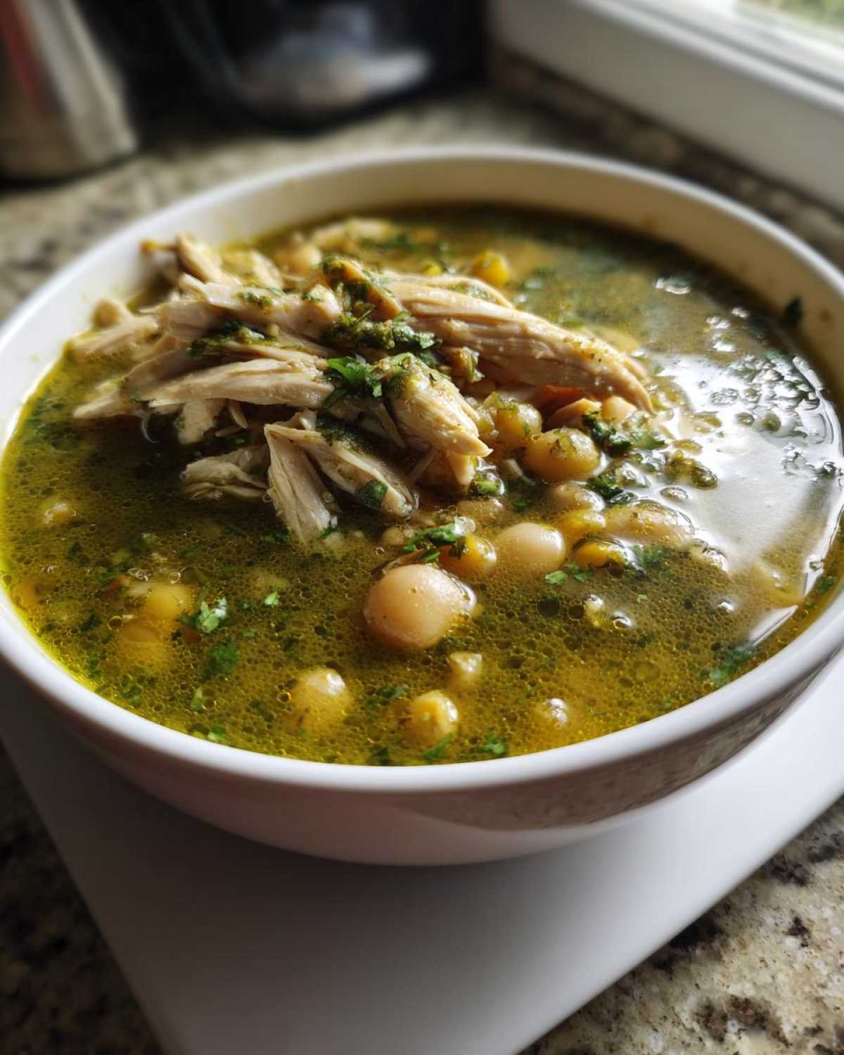A close-up of a white bowl filled with vibrant green chicken pozole, featuring shredded chicken and hominy kernels in a flavorful broth.