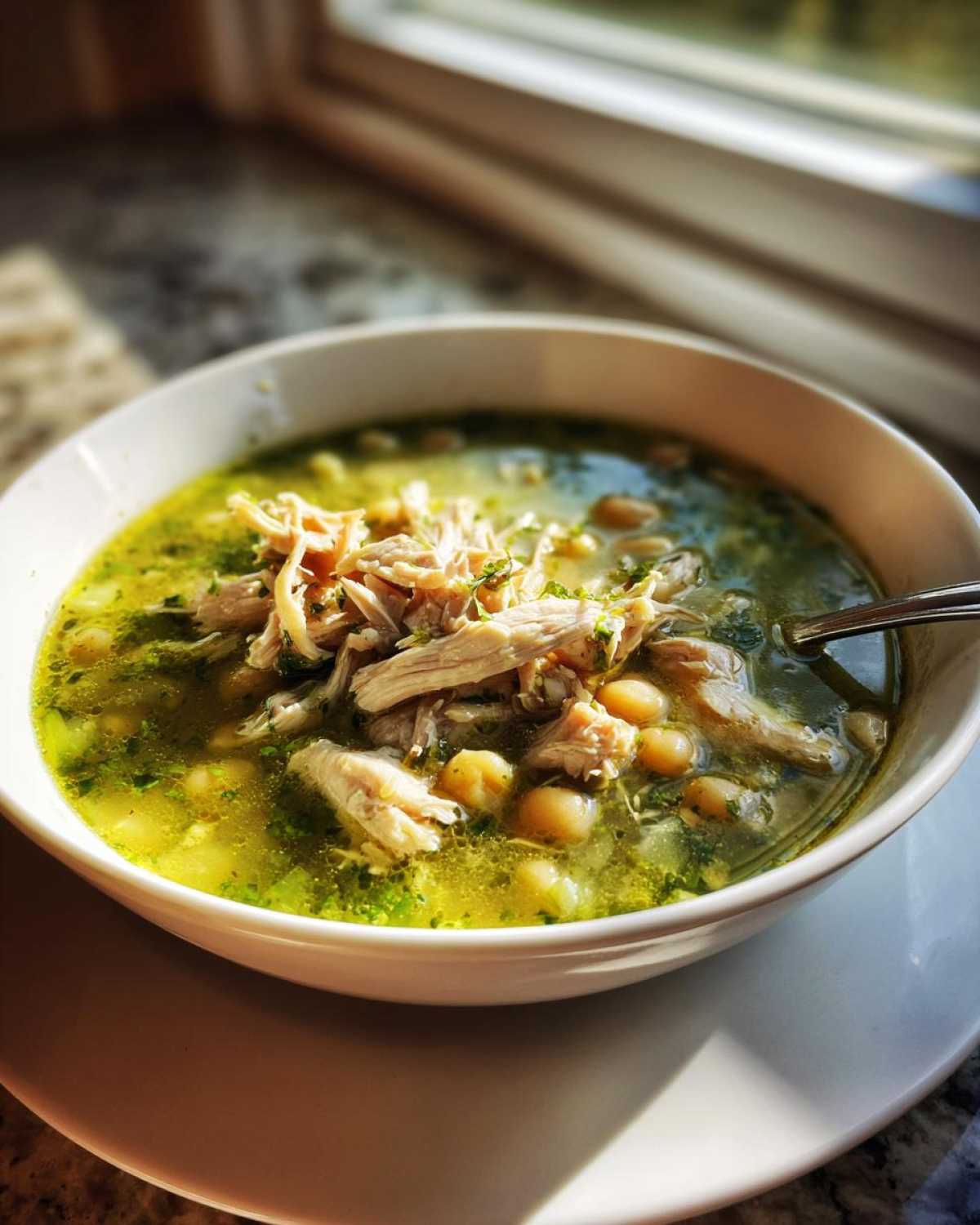 A close-up of a white bowl filled with vibrant green chicken pozole, featuring shredded chicken and hominy kernels.