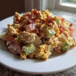 A mound of creamy blt chicken salad mixed with chunks of tomato, avocado, and topped with crispy bacon bits on a white plate.