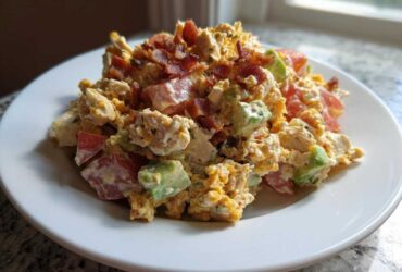 A mound of creamy blt chicken salad mixed with chunks of tomato, avocado, and topped with crispy bacon bits on a white plate.