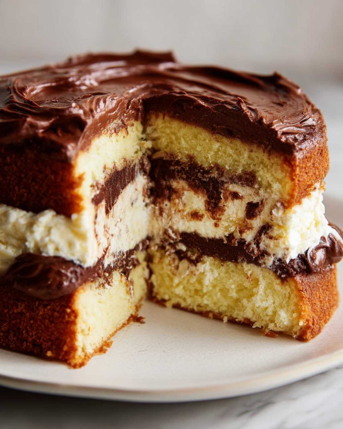 A slice cut from a layered Italian Love Cake showing yellow cake, white cream, and dark chocolate frosting layers.