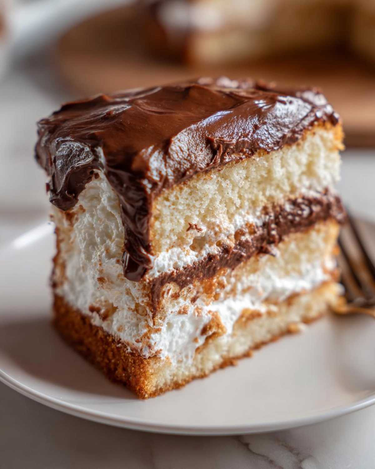 Close-up of a layered slice of Italian love cake featuring sponge, white filling, and rich chocolate frosting.