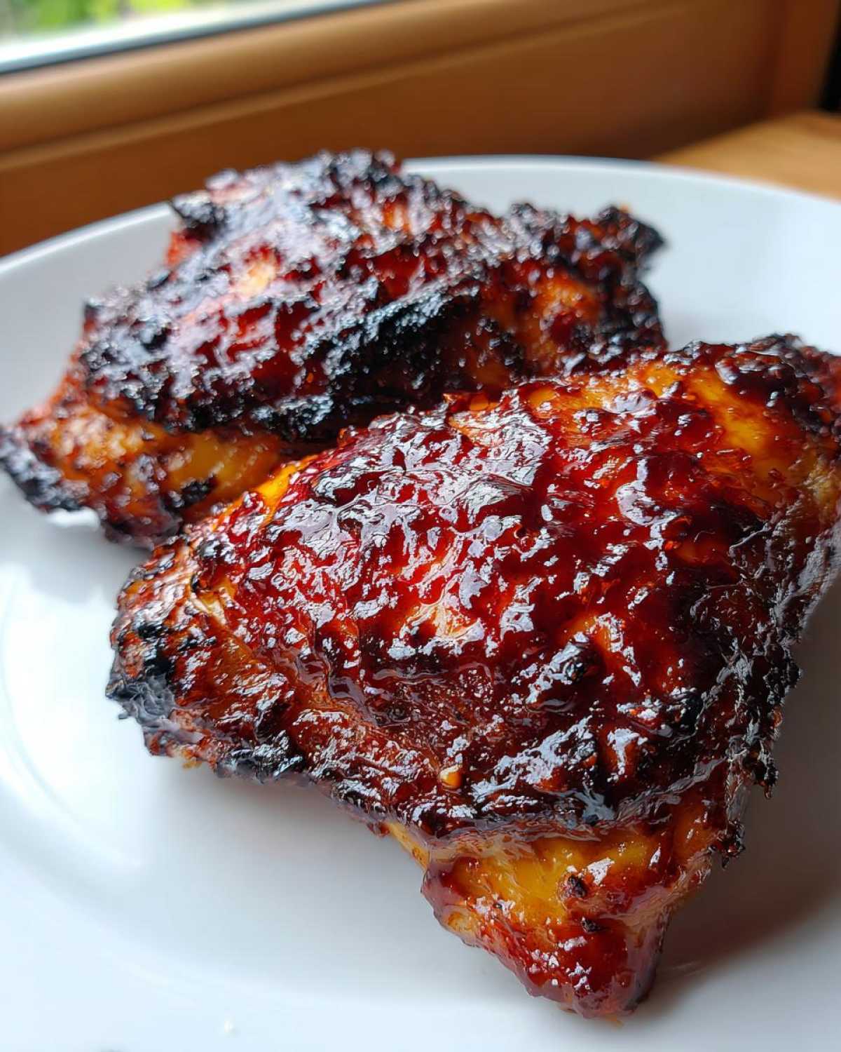 Close-up of two pieces of perfectly cooked bbq chicken with a thick, caramelized, and slightly charred glaze.