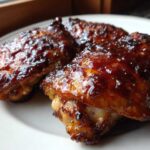 Close-up of three pieces of juicy bbq chicken wings covered in a thick, glossy, dark brown sauce.