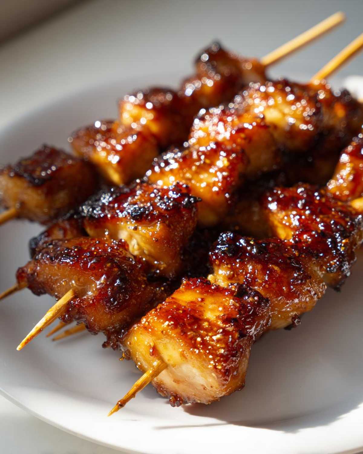Close-up of several juicy chicken skewers coated in a dark, glistening glaze resting on a white plate.