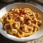 A bowl of rich Marry Me Chicken Pasta featuring fettuccine, chunks of chicken, and sun-dried tomatoes in a creamy sauce.