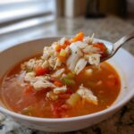 A spoonful of rich maryland crab soup showing large flakes of white crab meat, carrots, and celery being lifted from a white bowl.