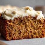 Close-up of a moist slice of applesauce cake topped with thick, creamy white frosting.