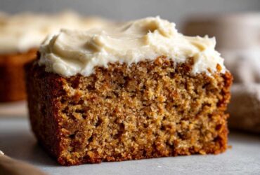 Close-up of a moist slice of applesauce cake topped with thick, creamy white frosting.