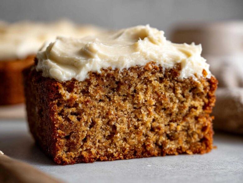 Close-up of a moist slice of applesauce cake topped with thick, creamy white frosting.