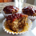 Close-up of a delicious mini meatloaf, one bitten to show the moist interior and sweet glaze topping.