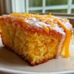 Close-up of a moist slice of orange juice cake topped with white glaze and fresh orange zest.
