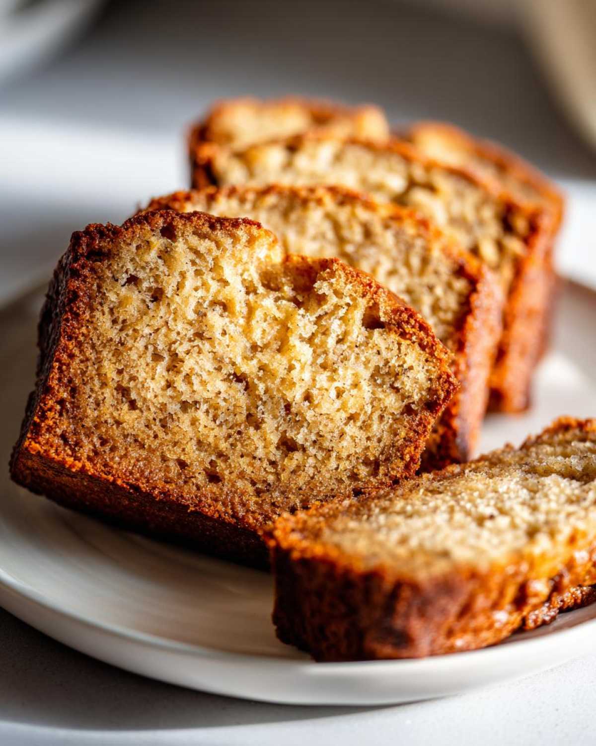 Close-up of moist, golden-brown slices of the best banana bread arranged on a white plate.