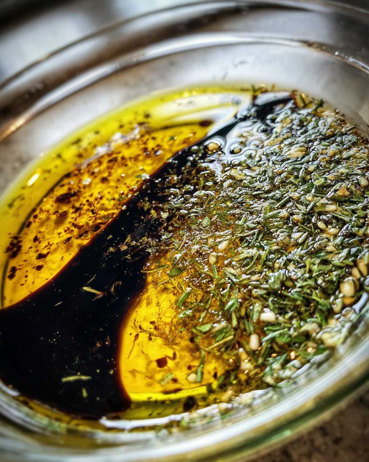Close-up of olive oil bread dip ingredients: olive oil, balsamic vinegar, and herbs/garlic.