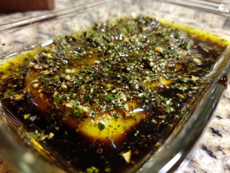 Close-up of olive oil bread dip ingredients, including olive oil, balsamic vinegar, garlic, and herbs, ready for mixing.