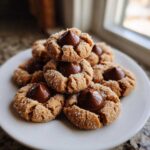 A stack of freshly baked peanut butter blossom cookies, rolled in sugar and topped with a rich chocolate kiss.