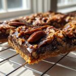 A close-up, sunlit view of a square piece of rich chocolate Pecan Pie Bark resting on a wire cooling rack.