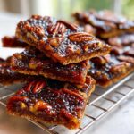 Close-up stack of gooey Pecan Pie Bark squares with whole pecans on top, cooling on a wire rack.