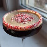 Close-up of a peppermint espresso martini with a thick foam top and a crushed candy cane rim.