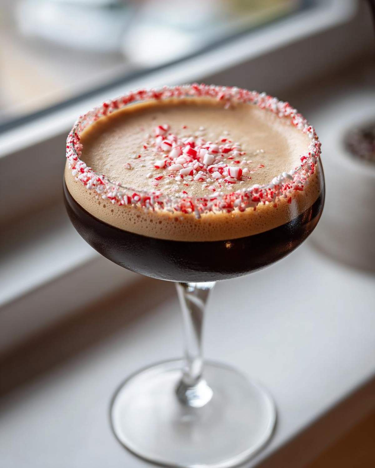 A rich, dark peppermint espresso martini garnished with a crushed candy cane rim and topping.