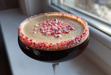 Close-up of a peppermint espresso martini with a thick foam top and a crushed candy cane rim.