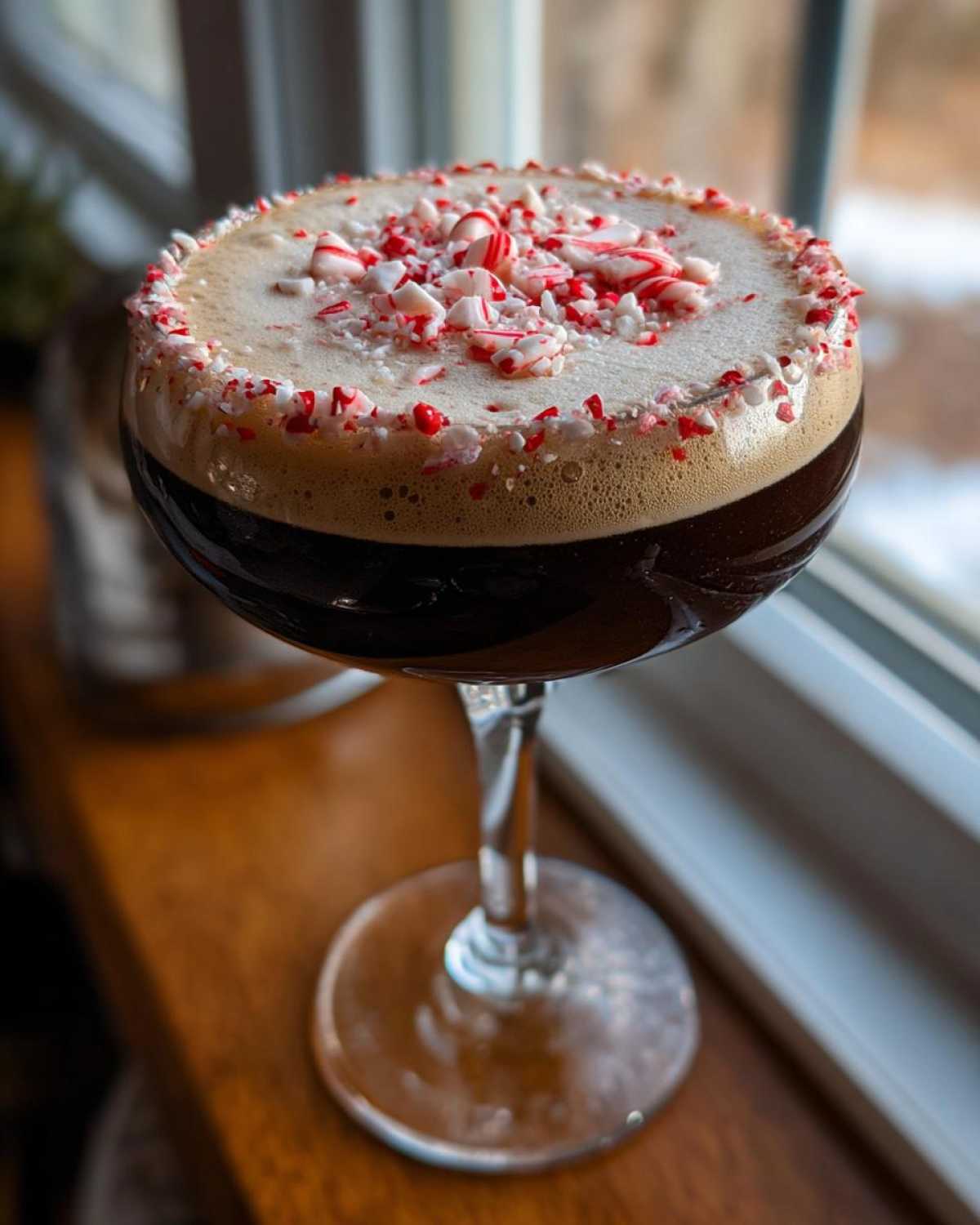 A rich peppermint espresso martini in a coupe glass, garnished with crushed candy canes on the foam.