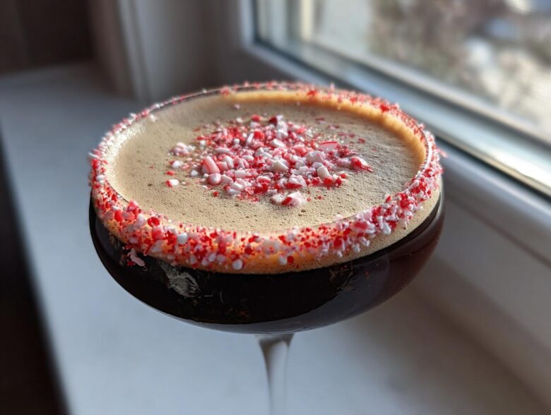 Close-up of a peppermint espresso martini with a thick foam top and a crushed candy cane rim.