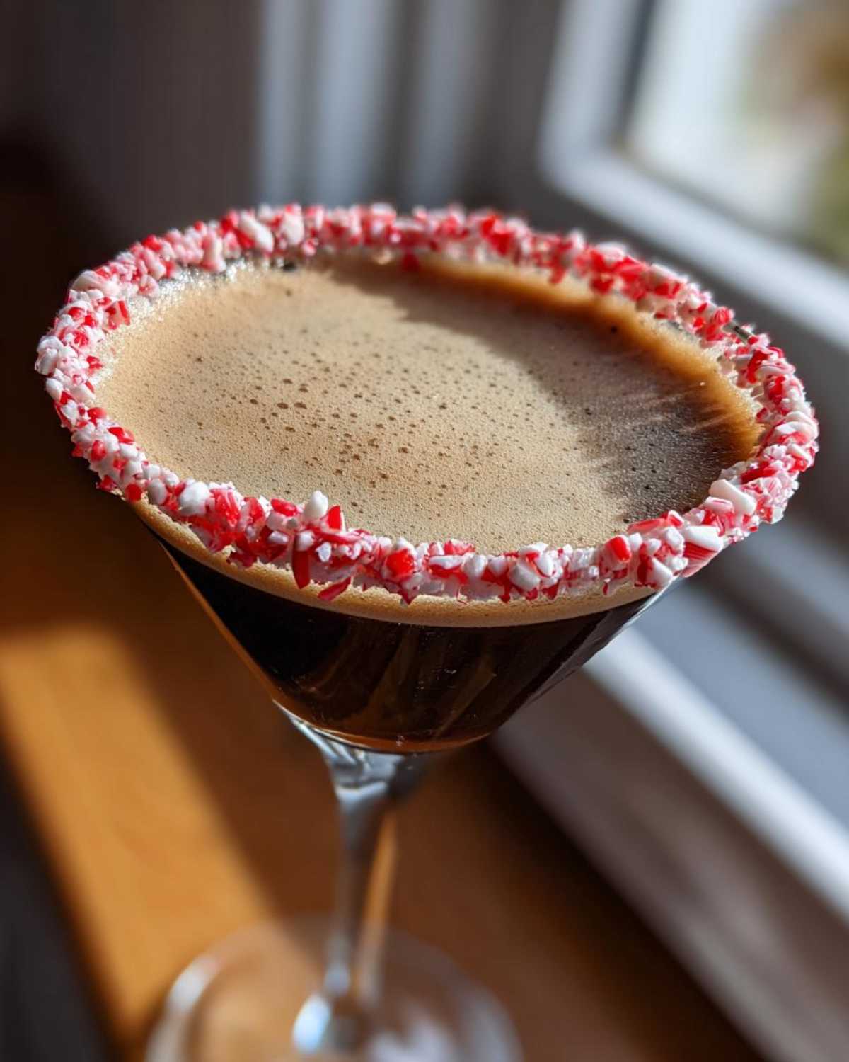 Close-up of a peppermint espresso martini in a coupe glass with a crushed candy cane rim.