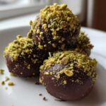 Close-up of four rich, dark chocolate balls coated in bright green crushed pistachios, representing dubai chocolate balls.