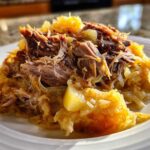 Close-up of tender, shredded pork served over a mound of golden pork and sauerkraut on a white plate.