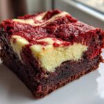 A single, decadent slice of red velvet cheesecake brownies showing the dark brownie base and swirled red and cream cheese topping.