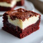 A decadent square of red velvet cheesecake brownies showing a rich red bottom layer and a creamy white cheesecake swirl on top.